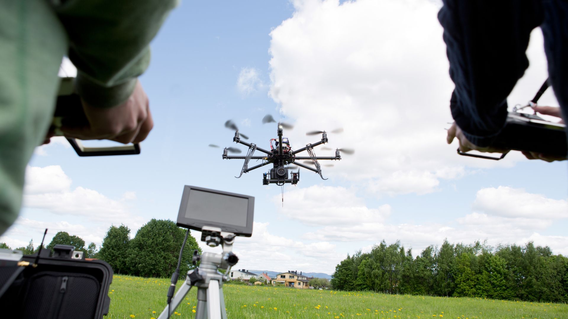 Hexacopter drone flying over grassy field with monitor and controllers